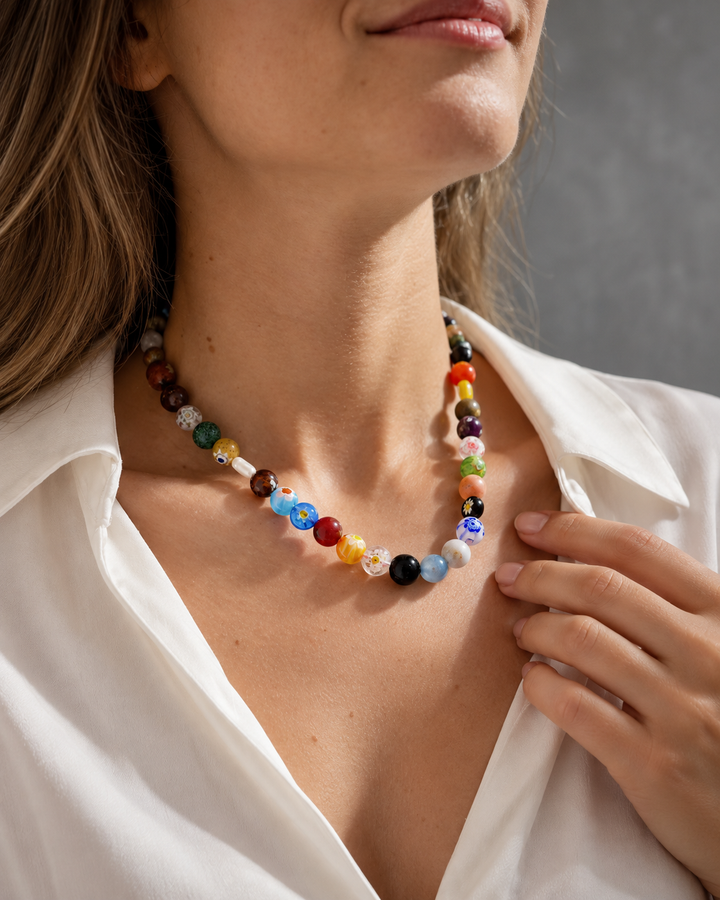 Collar de cuentas multicolores sostenido con la mano sobre una camisa blanca.