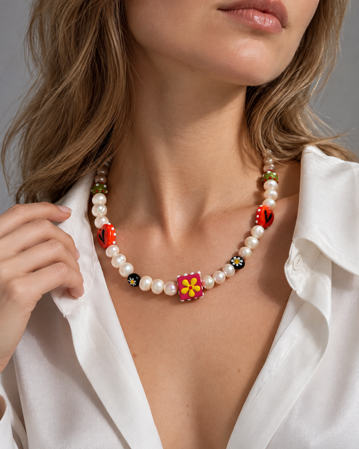 Collar de cuentas claras con elementos rojos y una pieza cuadrada decorada con una flor amarilla.