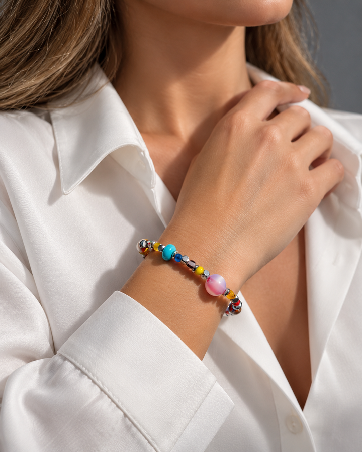 Pulsera de cuentas de colores con una cuenta rosada y otra turquesa en una muñeca sobre una camisa blanca.