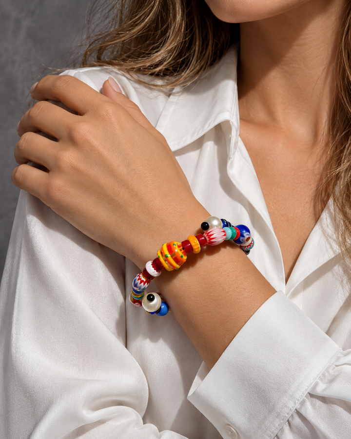 Pulsera multicolor de cuentas variadas en la muñeca, con el brazo cruzado sobre una camisa blanca.