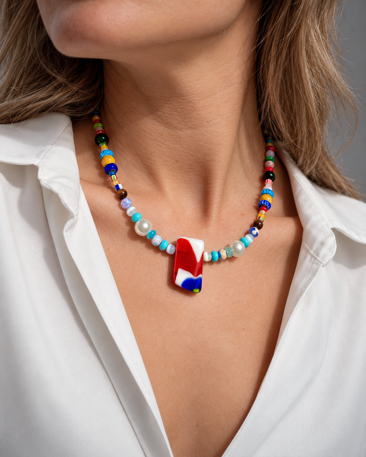 Collar de cuentas multicolores con un colgante rectangular rojo, blanco y azul.
