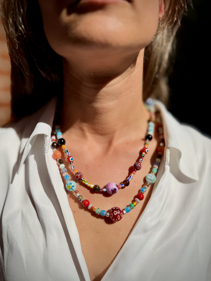Composición de dos líneas de cuentas multicolores, con elementos centrales en tonos violeta y rojo.