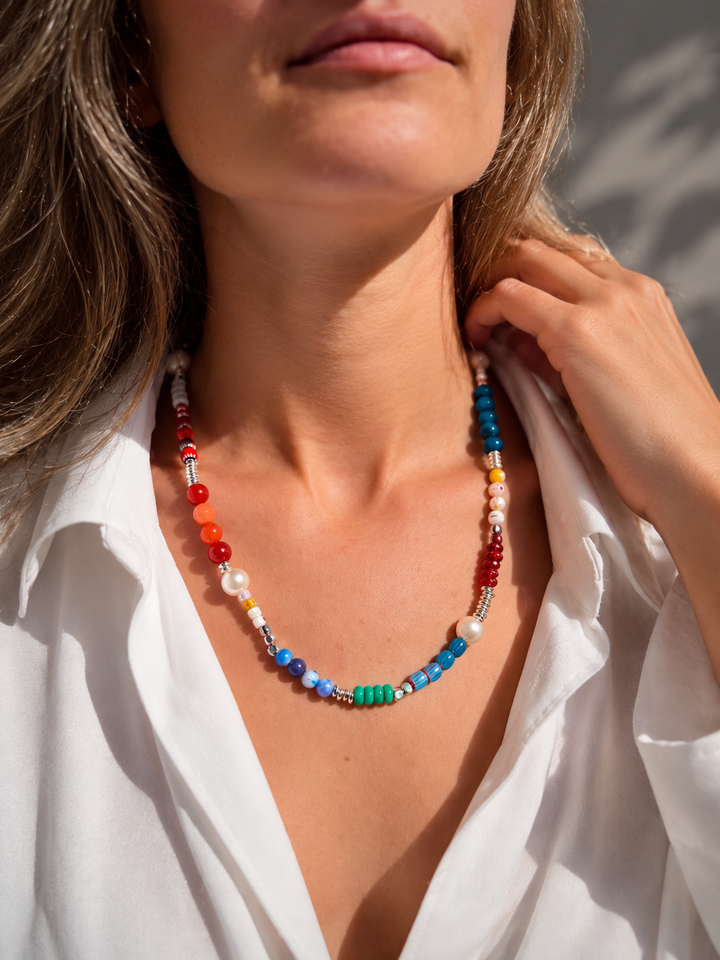 Collar largo de cuentas pequeñas azules, verdes, rojas y claras, dispuesto en una sola línea.
