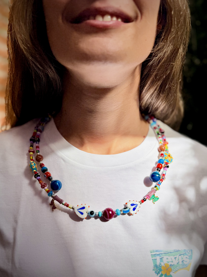 Collar multicolor con formas blancas de detalles azules y una cuenta central violeta sobre una camiseta blanca.